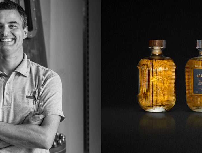 Person standing next to three bottles of The Hearach whisky on a black background