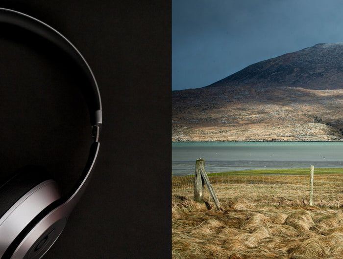 Pair of headphones on a dark background with a scenic landscape featuring mountains and water.
