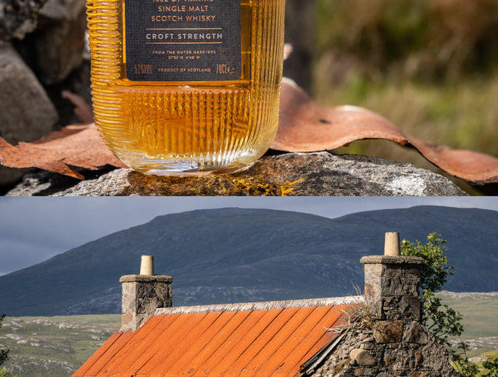 Bottle of The Hebrach whisky in front of a stone cottage with a red roof in a scenic landscape.
