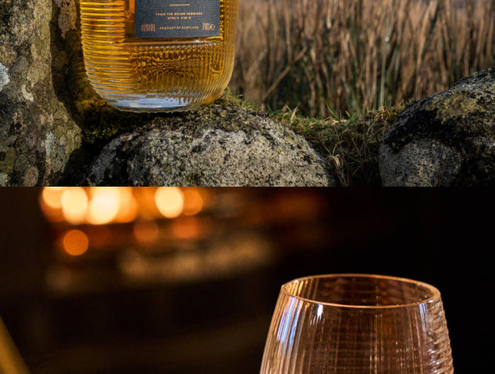Bottle of The Hearach whisky on a rock with a scenic background, followed by a hand holding a glass of whisky.