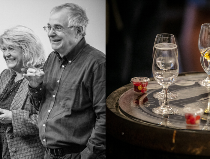 Two people enjoying a drink together with a table of glasses and drinks in the background.